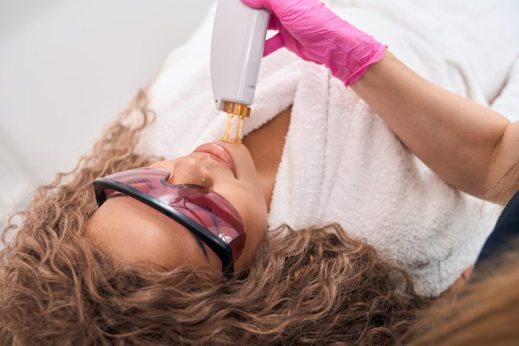 Woman lies on a couch in protective glasses for a laser hair removal procedure